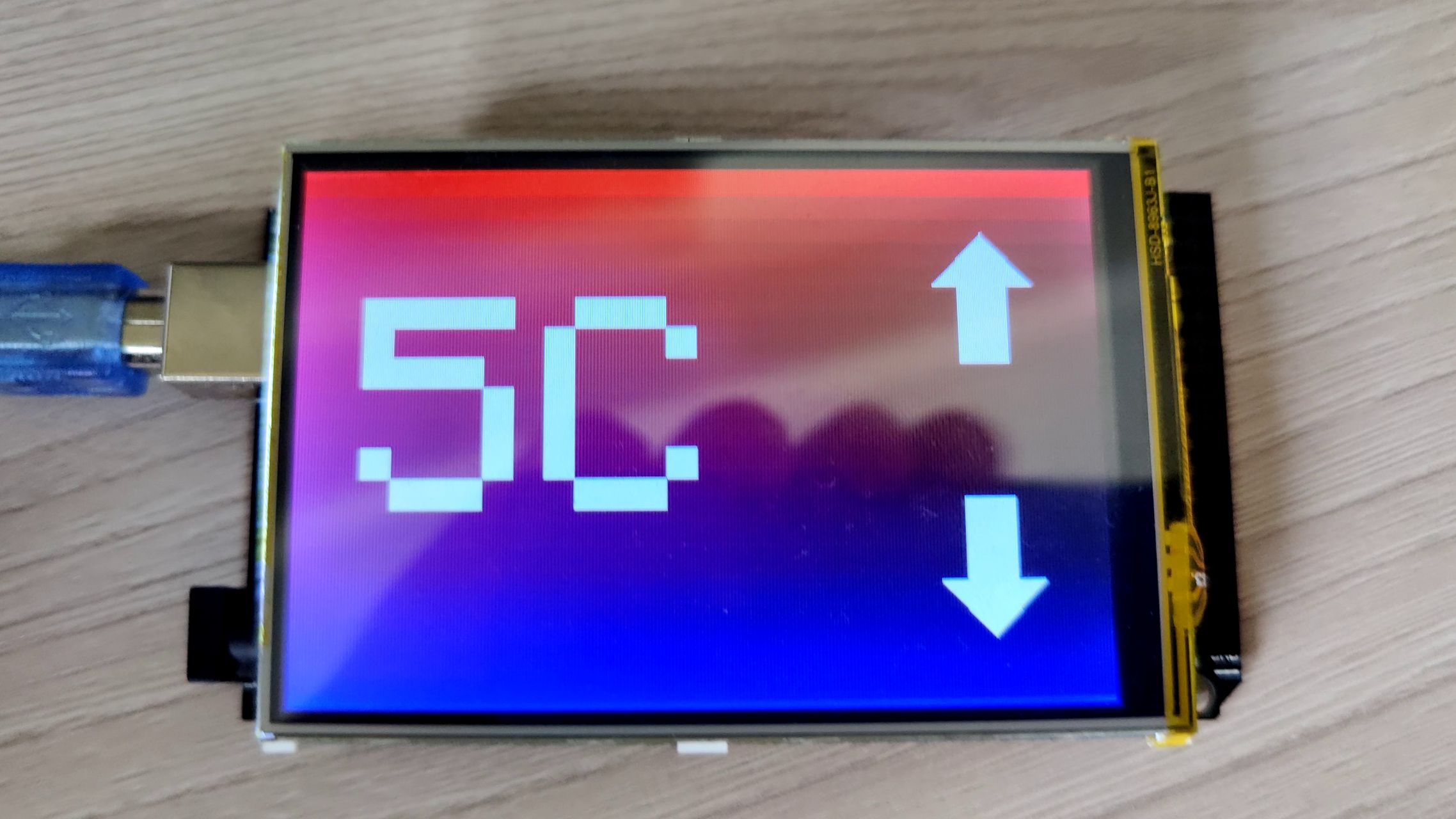 Arduino Uno with an LCD breakout. LCD is showing "5C" on the left and two arrows on the right pointing up and down. In the background is a vertical red-blue gradient.